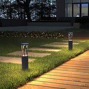 Row of modern black mushroom cap bright path lights illuminating a stone walkway and lush green grass at night.