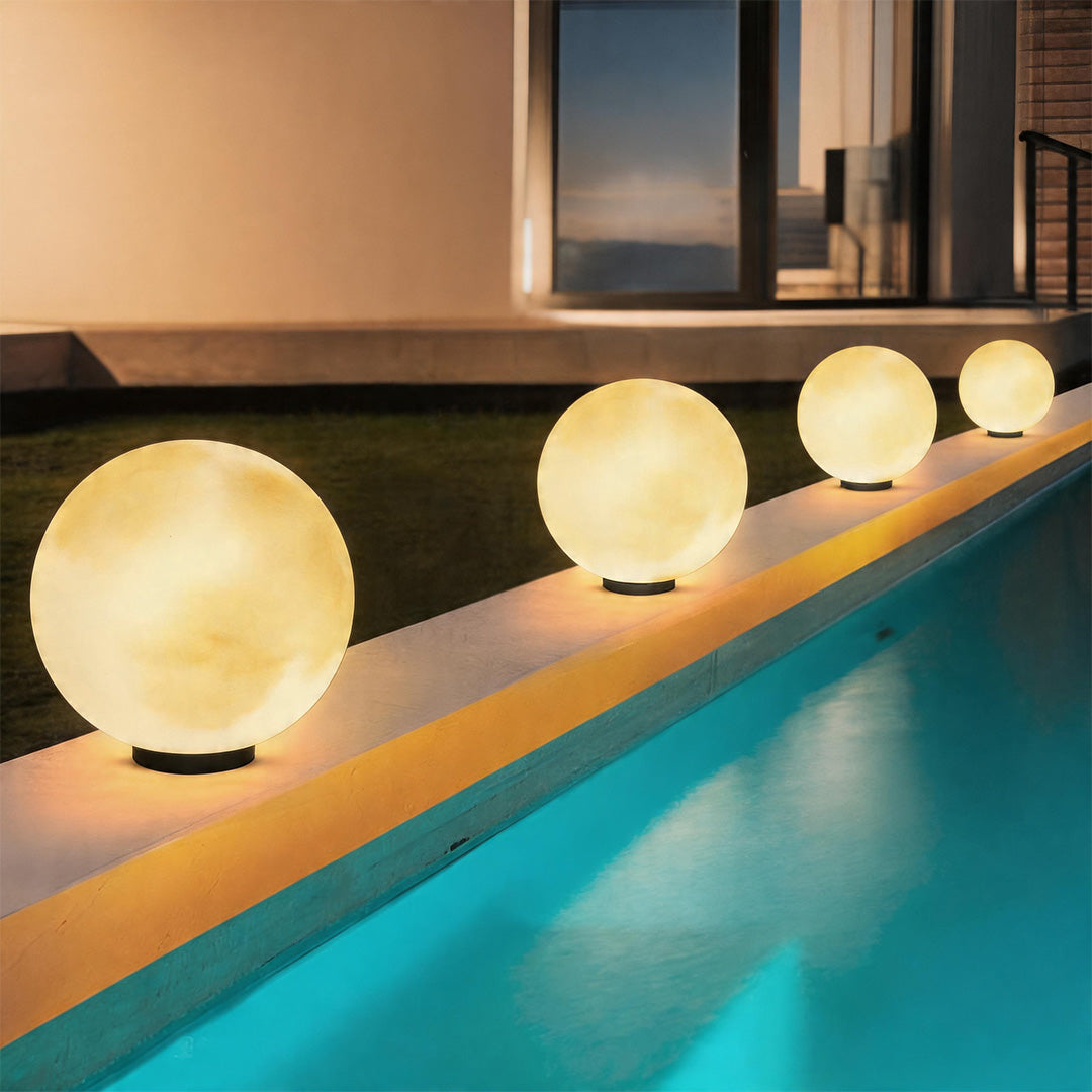 Row of moon pillar lights glowing along the edge of a luxury swimming pool during the night.