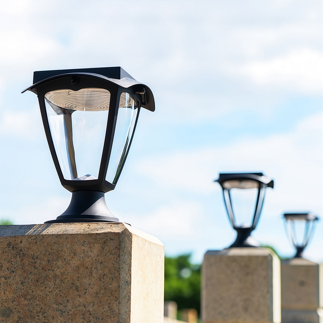 Row of black solar light pillar fixtures installed on granite posts, shown against a bright sky.