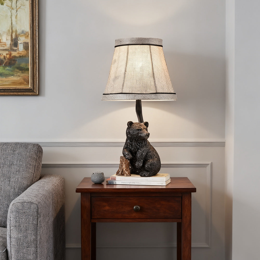 Rustic resin table lamp featuring a black bear base and textured gray fabric shade, placed on a dark wood end table next to a sofa.