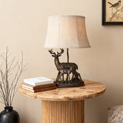 Rustic deer table lamp featuring a bronze stag and fawn figurine base and a natural linen tapered shade.
