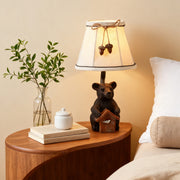 Rustic bear table lamp featuring a carved bear base holding a small birdhouse, styled on a wooden nightstand with fresh greenery.