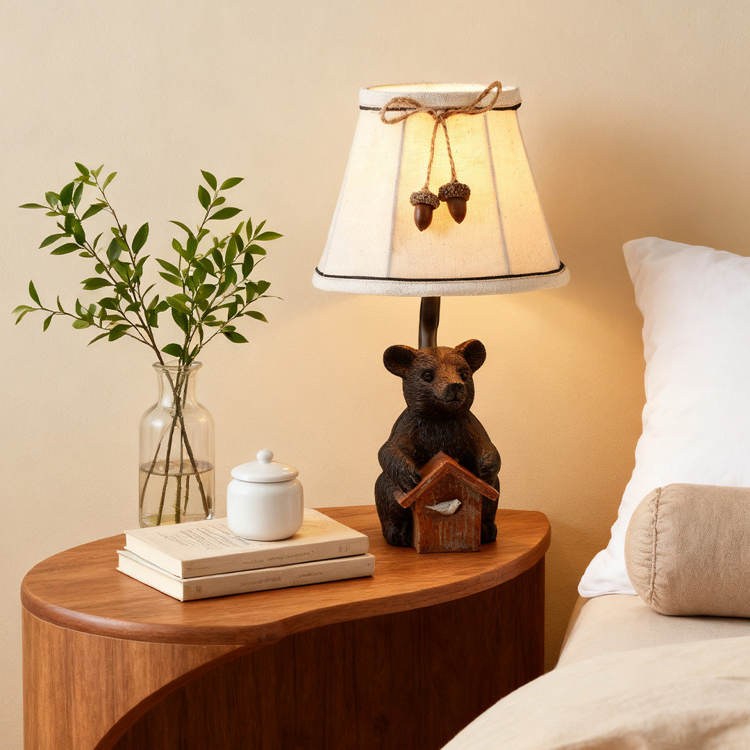 Rustic bear table lamp featuring a carved bear base holding a small birdhouse, styled on a wooden nightstand with fresh greenery.