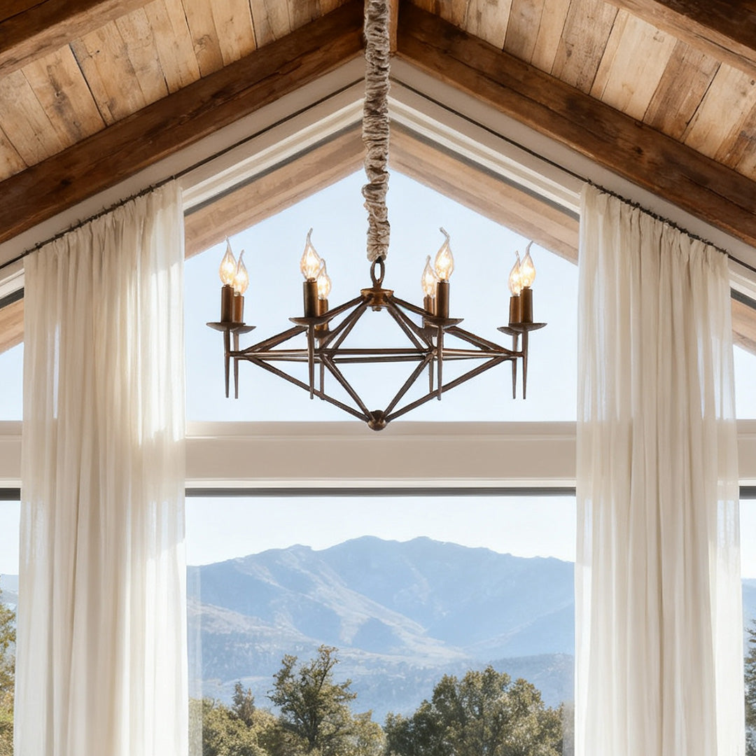 Rustic brown chandelier with a diamond-shaped iron frame and candle bulbs, suspended in a vaulted ceiling room with large scenic windows.