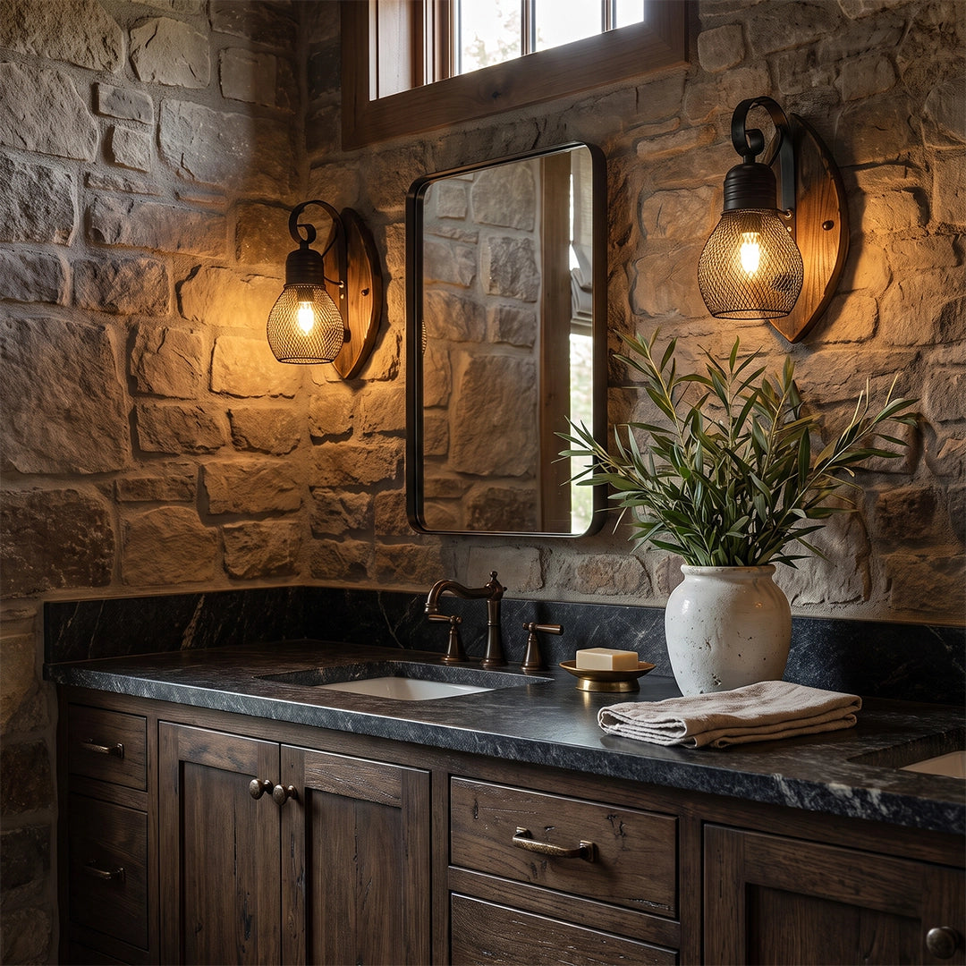 Rustic farmhouse wall sconce with a warm glowing bulb, black metal arm, and round wood backplate beside a bathroom mirror on a stone wall.