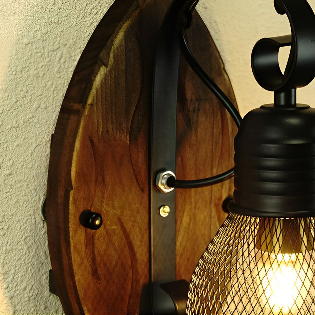 Rustic farmhouse wall sconce detail showing the wood backplate, black arm, and mesh bulb shade.