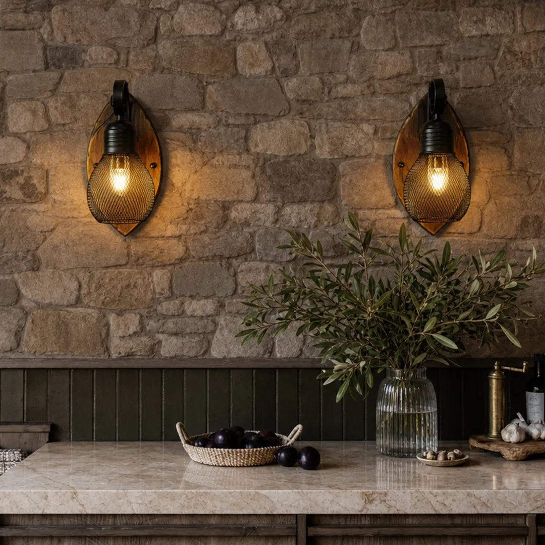 Rustic farmhouse wall sconce pair with warm textured glass bulbs and round wood backplates mounted on a stone wall above a kitchen counter.