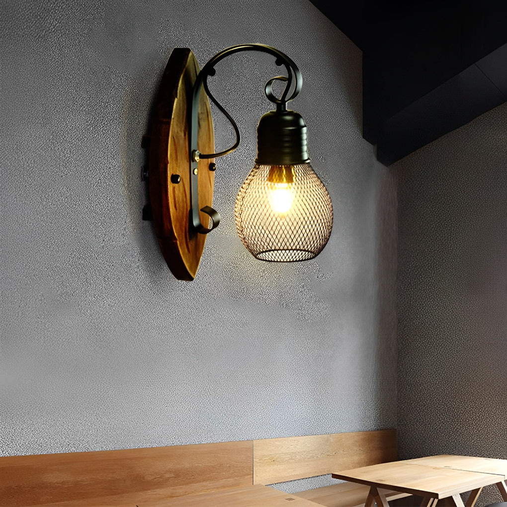 Rustic farmhouse wall sconce with a wood backplate and black mesh shade mounted beside a kitchen counter.