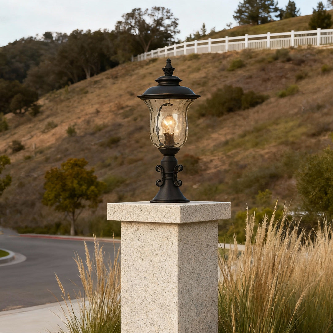 Rustic pillar gate light brightening textured stone column on hillside with natural landscaping