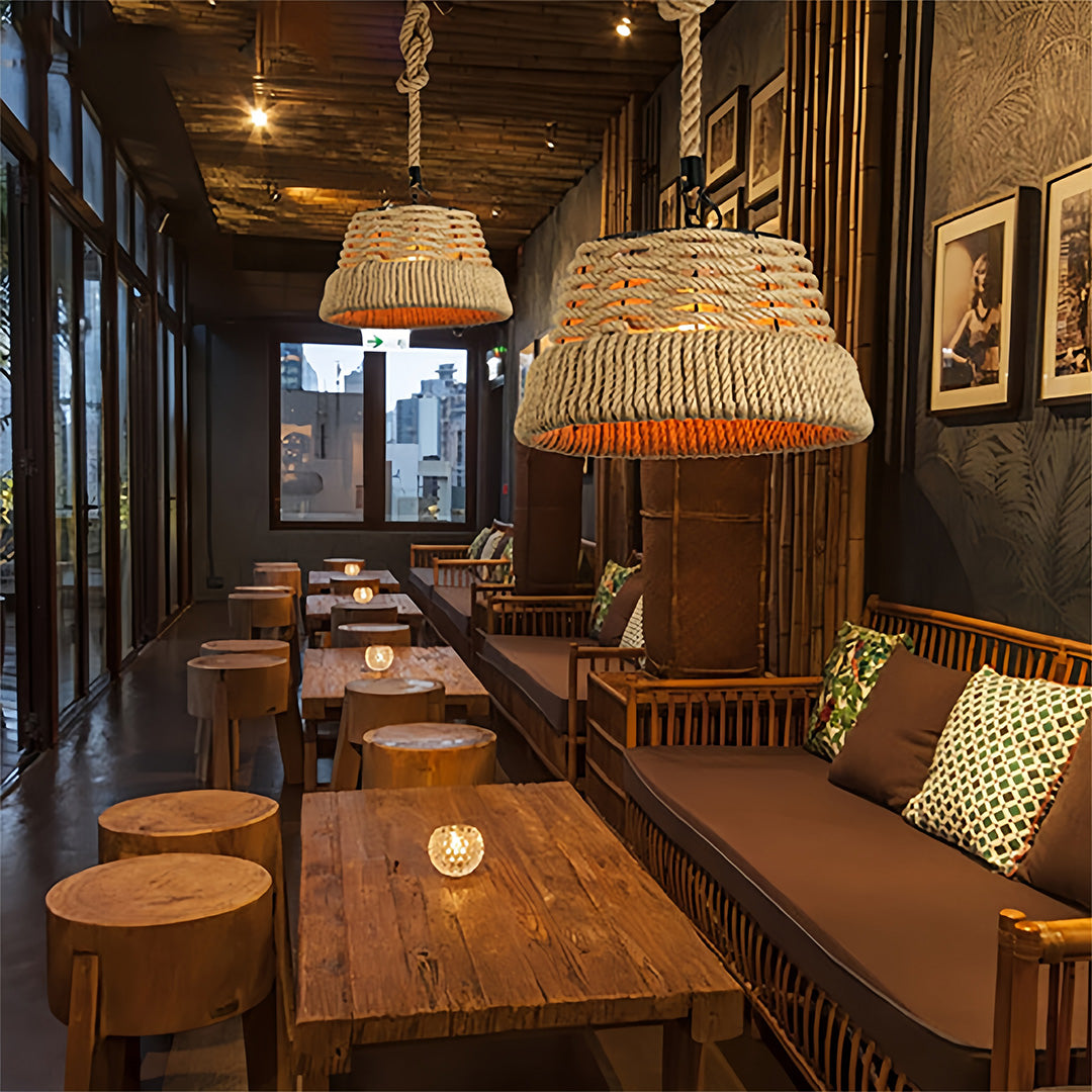 Rustic rope pendant lights hanging over dark wooden seating and tables in a long, sunlit cafe interior.
