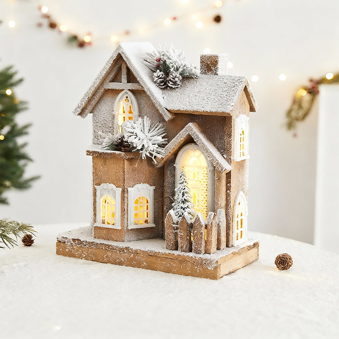 Rustic two-story cabin model among light up wooden christmas houses featuring a picket fence and trees.