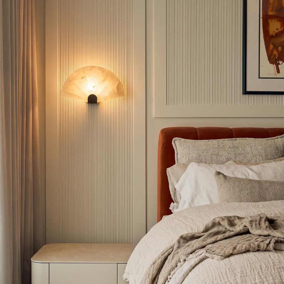 Scalloped wall sconce installed above a bedside table in a soft neutral bedroom.
