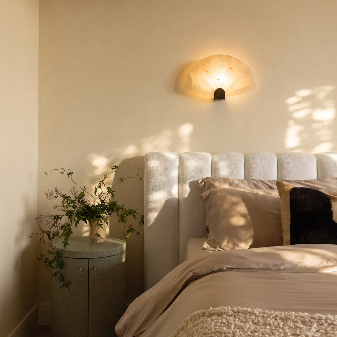 Scalloped wall sconce installed above a nightstand beside a bed with soft natural light.