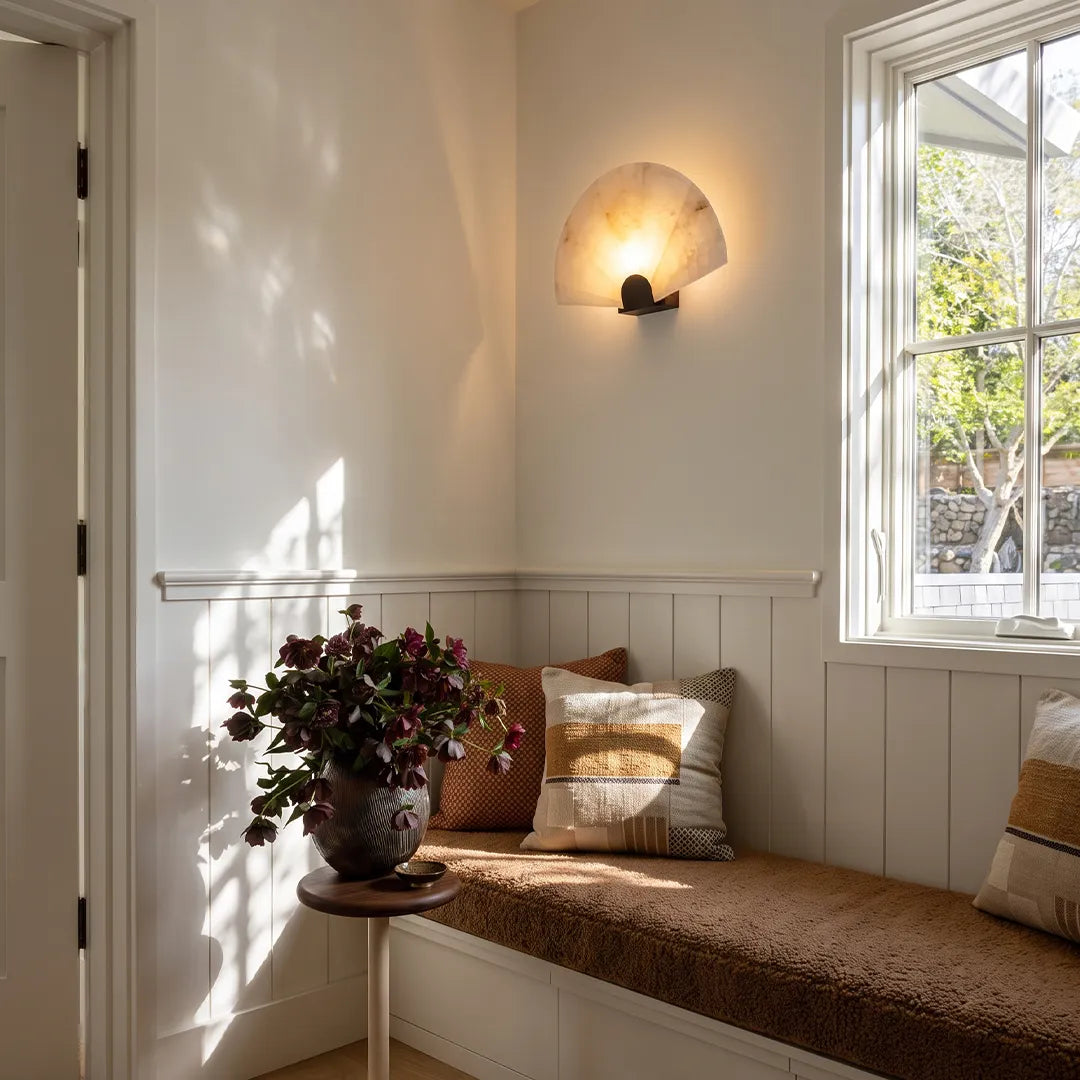 Scalloped wall sconce mounted above a window seat with cozy cushions and warm accent light.