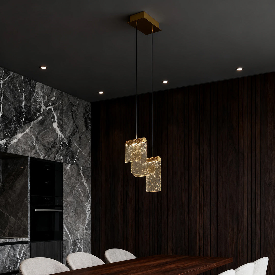 Sculptural gold pendant island light casting warm glow in moody room with black marble and dark curtains