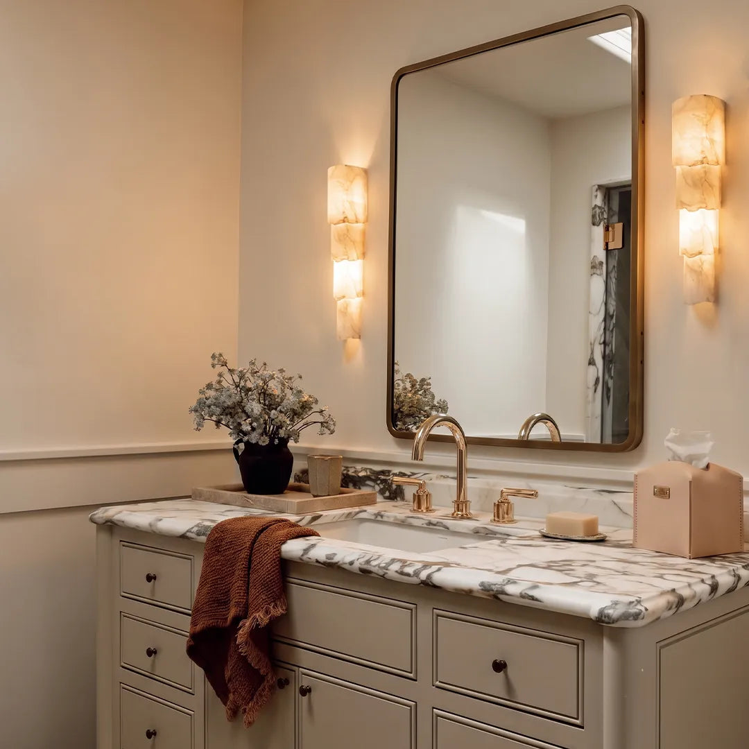 Sculptural wall sconce beside a bathroom mirror with layered alabaster-style panels and elegant warm illumination.