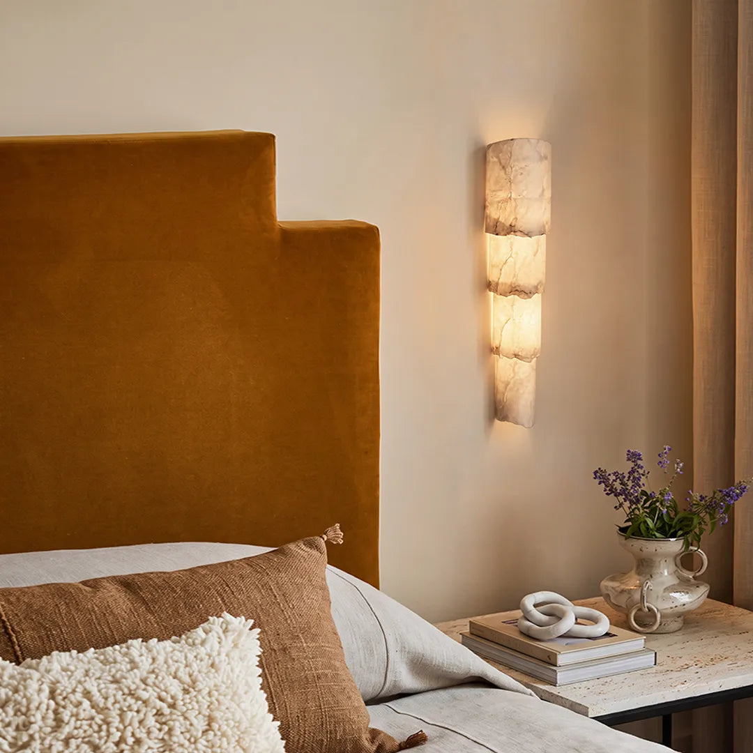 Sculptural wall sconce mounted beside a bed with layered alabaster-style panels and a warm ambient glow.