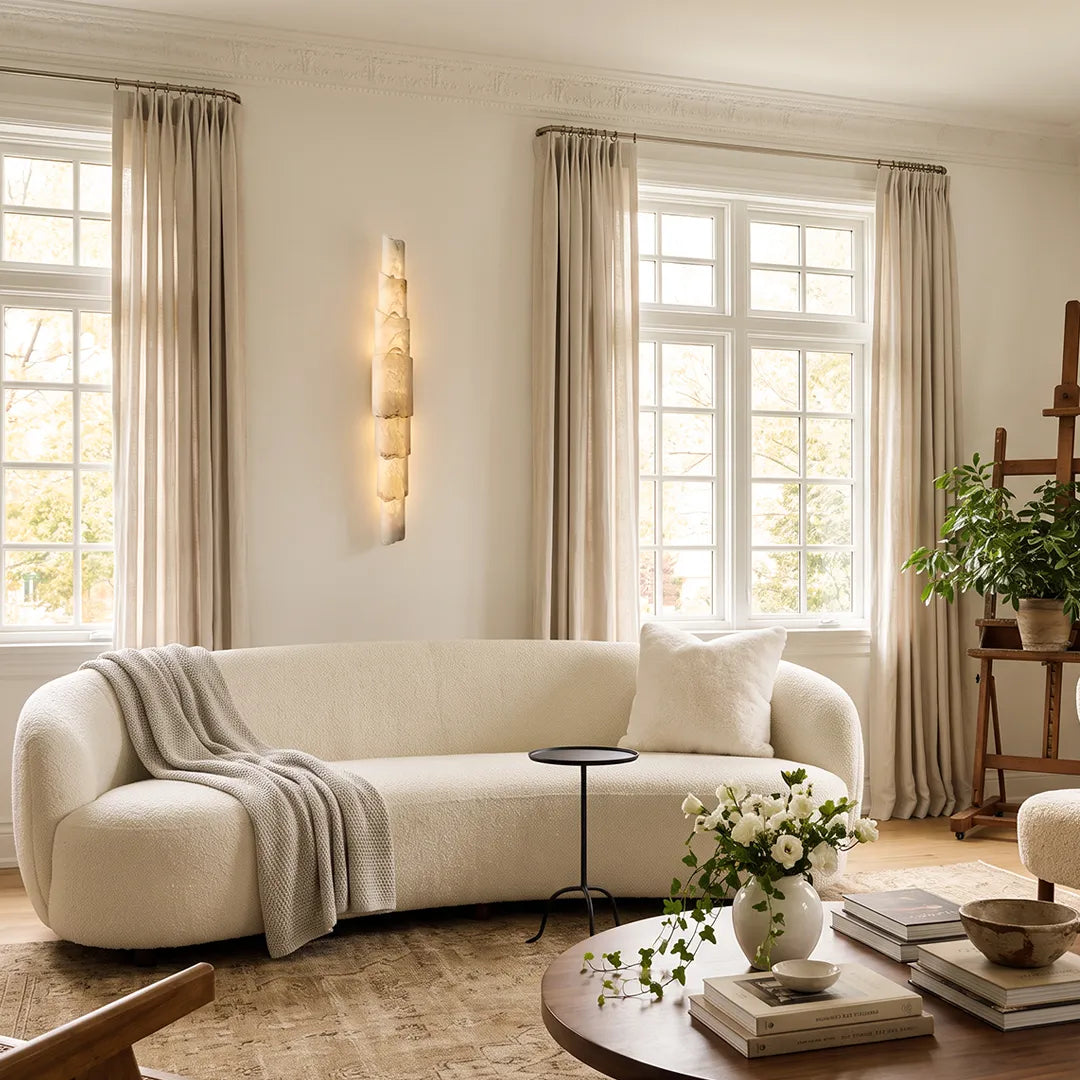 Sculptural wall sconce displayed in a bright living room with a curved sofa and warm vertical accent lighting.