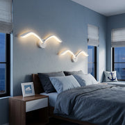 Seagull lighting sconces with wing-inspired curves mounted above a bed in a modern blue bedroom.