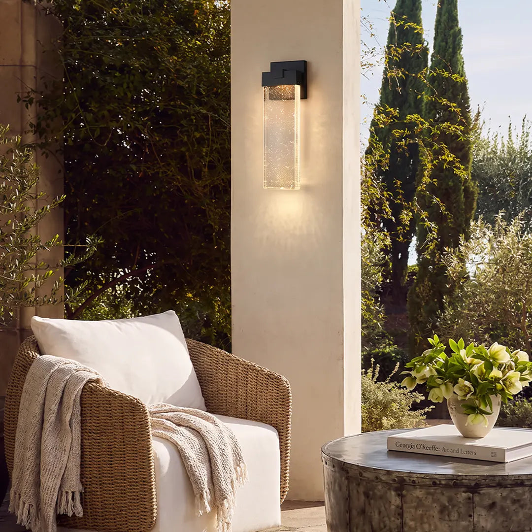 Seeded glass outdoor wall lighting installed beside a patio lounge area on a cream exterior column.