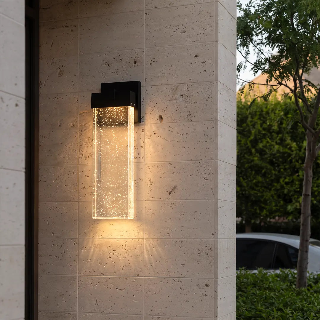 Seeded glass outdoor wall lighting mounted on a textured stone exterior wall, casting a warm glow downward.
