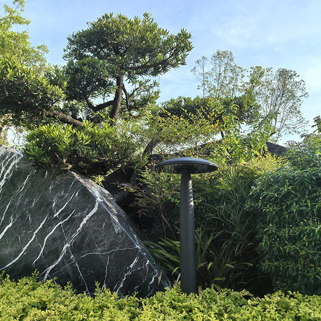 Sleek black mushroom bollard light in a serene garden, surrounded by trees and greenery.