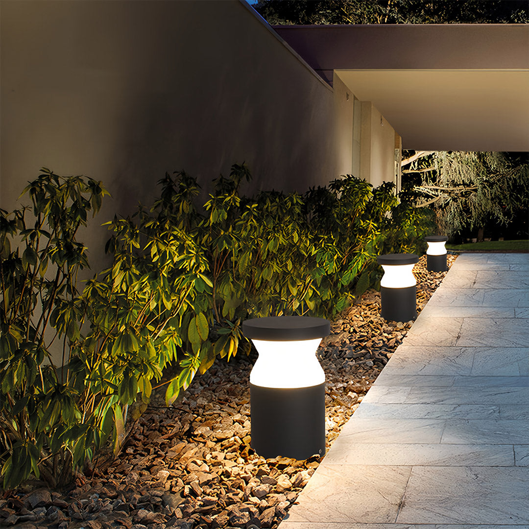 Set of low-profile modern path lights placed along the edge of a well-maintained garden bed and dark mulch.