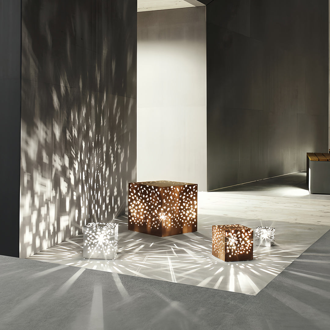 Perforated cube black outdoor lantern lights placed beside a wall, creating intricate shadow patterns.