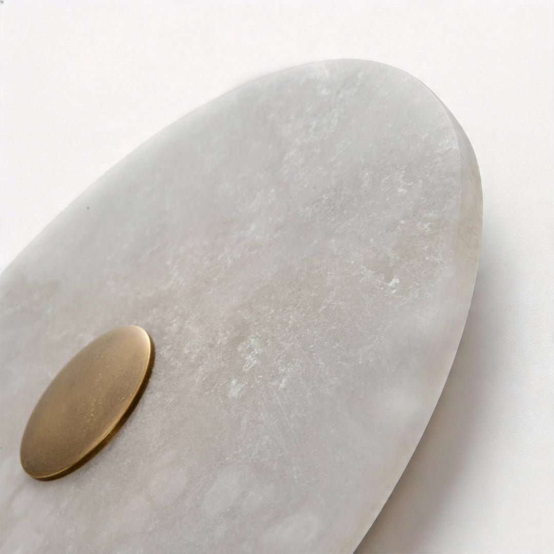 Side view of a round wall light showing the natural stone grain and brass mounting plate ok.
