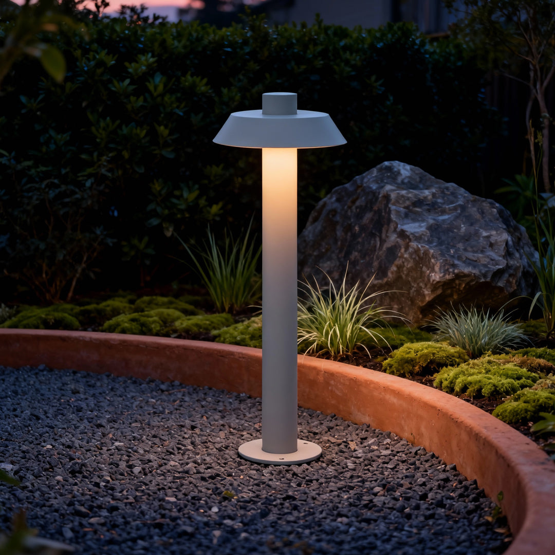 A group of silver aluminum path lights placed beside a landscaped garden path during dusk.
