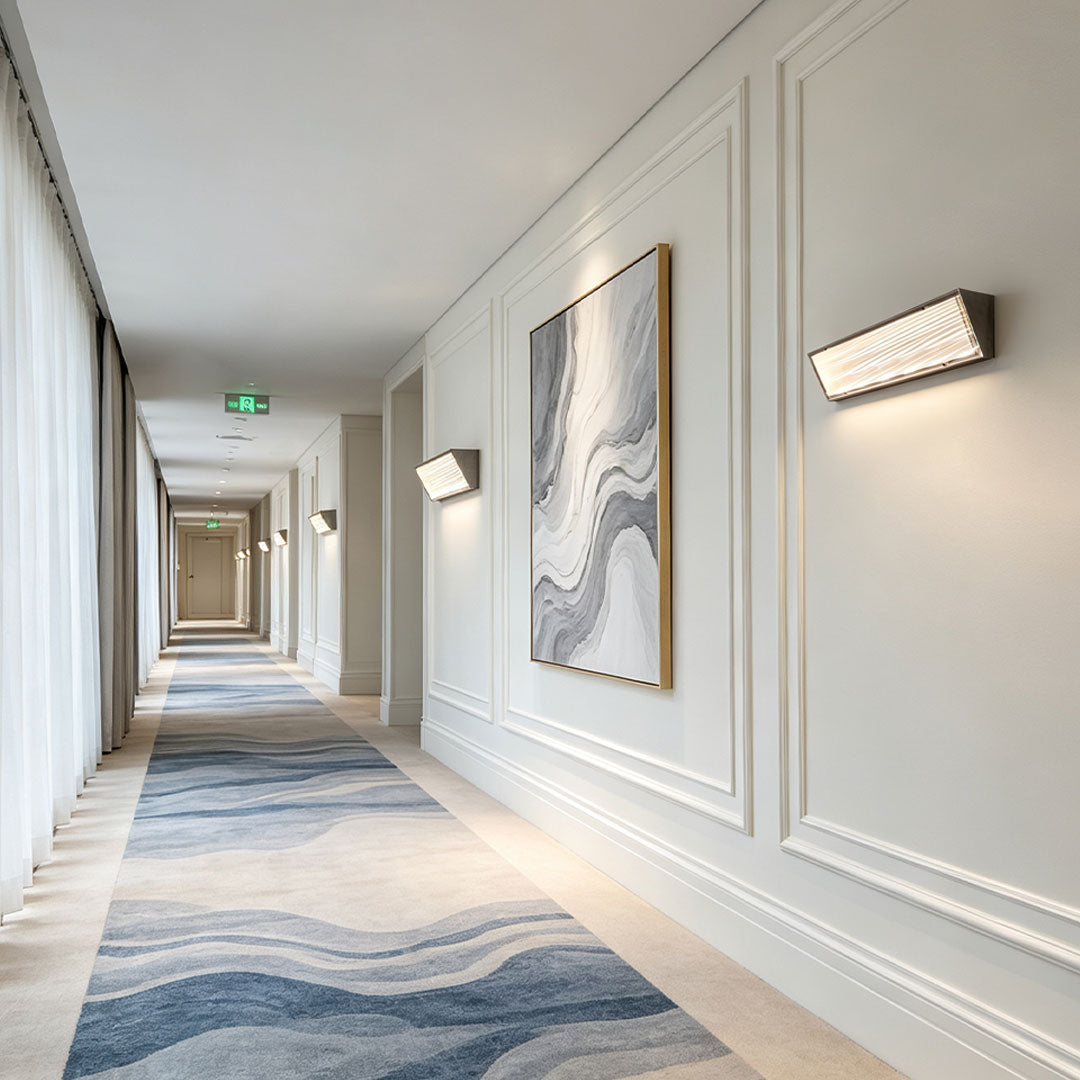 Minimalist silver wall lights illuminating a sophisticated hotel hallway with elegant white wall panel detailing.