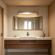 Modern silver wall lights above a wooden vanity mirror creating warm illumination in a minimalist bathroom interior.