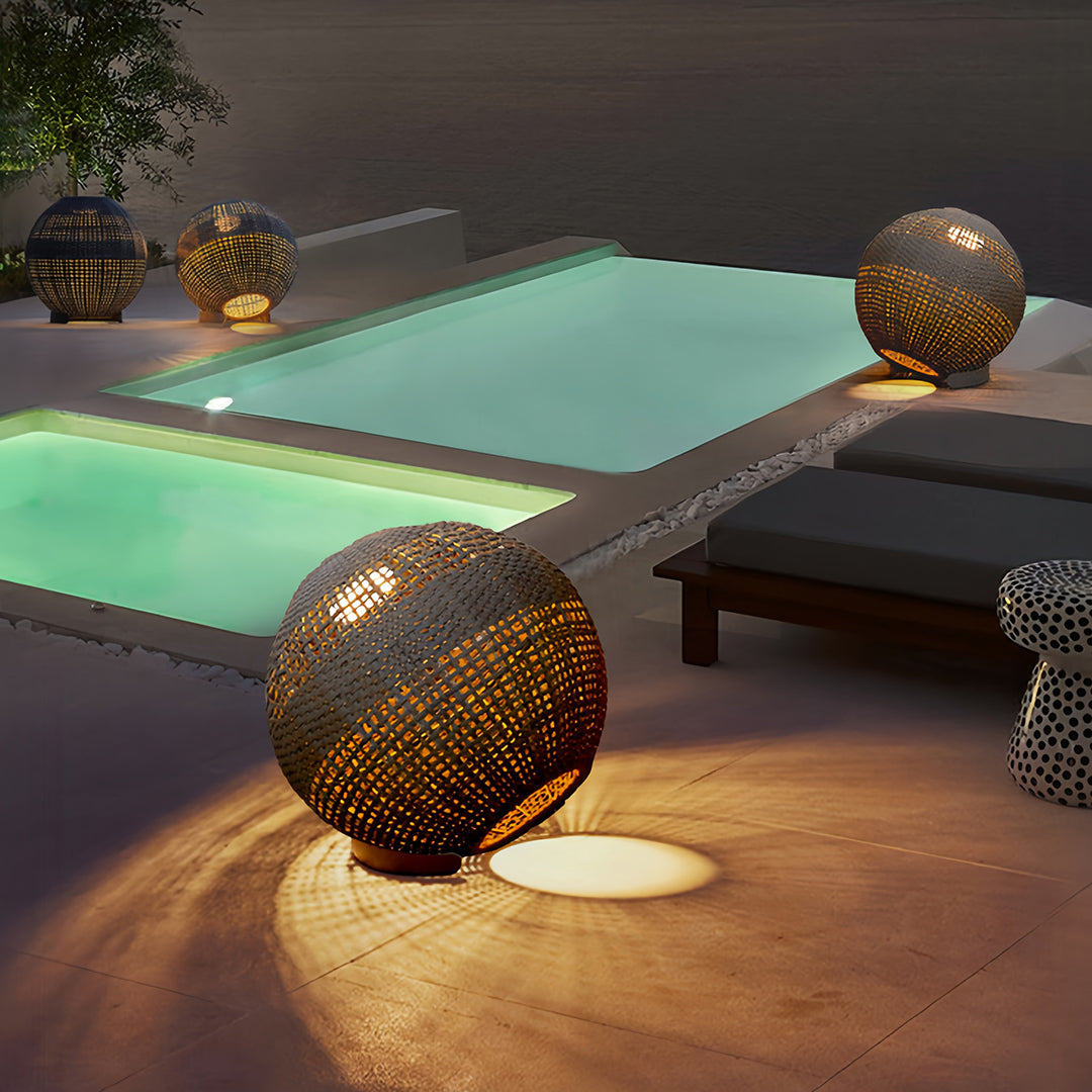 Single large outdoor globe lantern providing subtle accent lighting next to a swimming pool and dark lounge chairs.