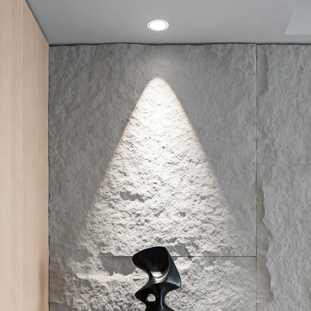 Single accent spotlight creating dramatic wash lighting on textured grey wall with sculpture display