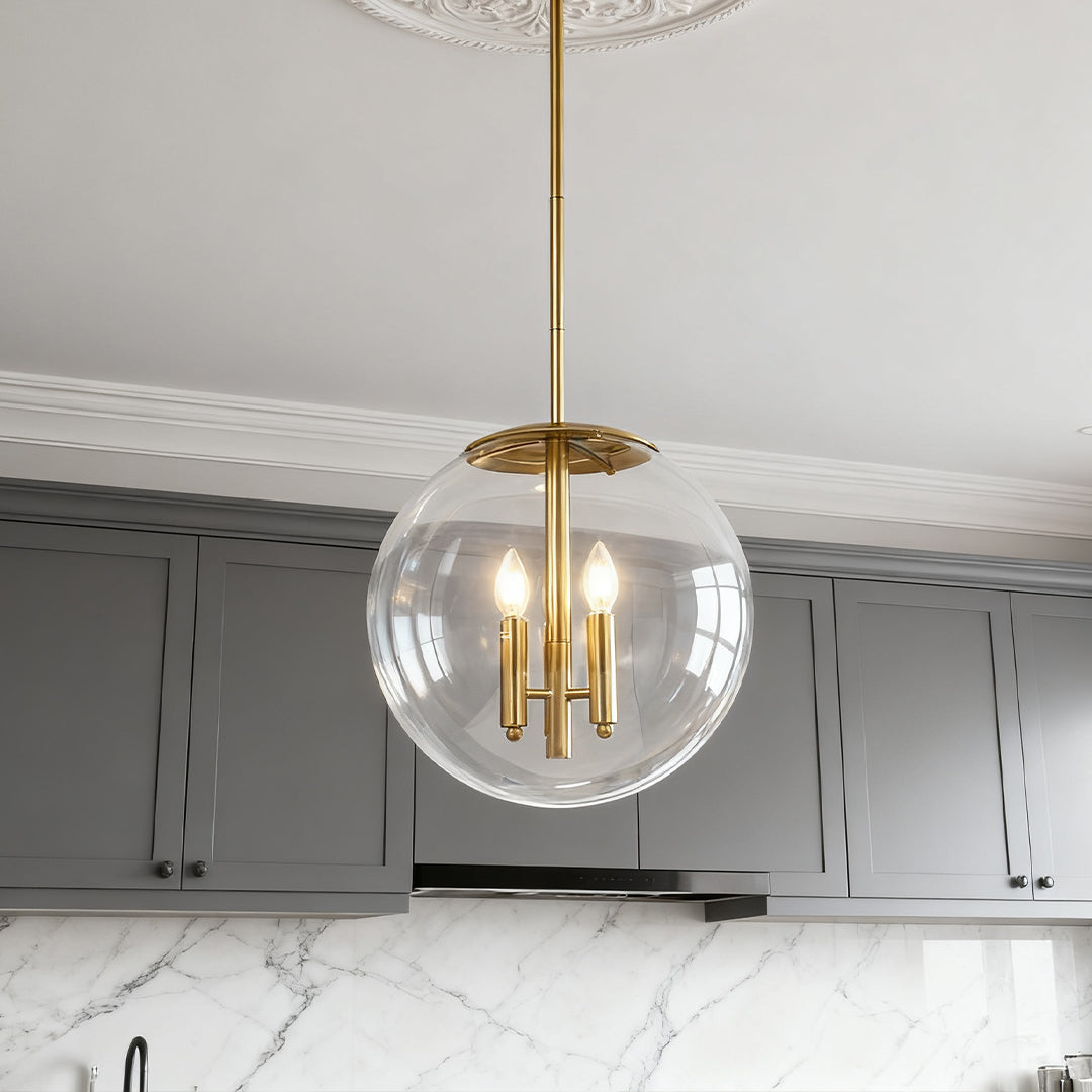 A single modern clear globe pendant light with brass rod suspension illuminating a sleek gray kitchen area.