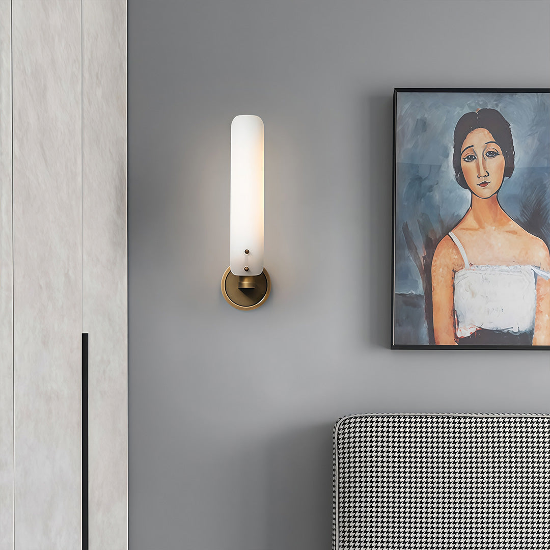 Single brass wall light with glass shade brightening minimalist hallway with framed portrait.