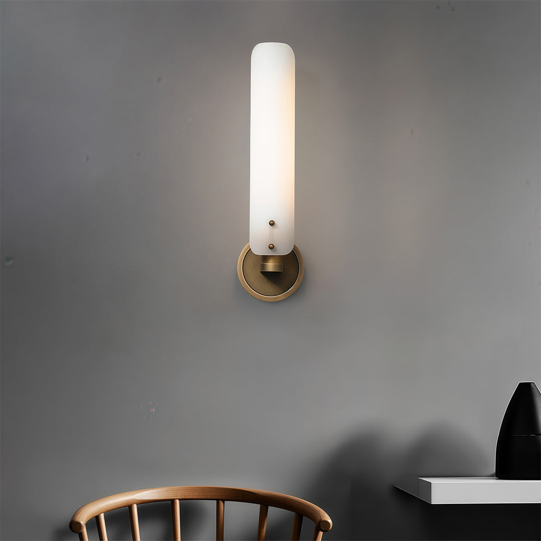 Single brass wall light with glass shade creating warm ambient lighting on grey interior wall.