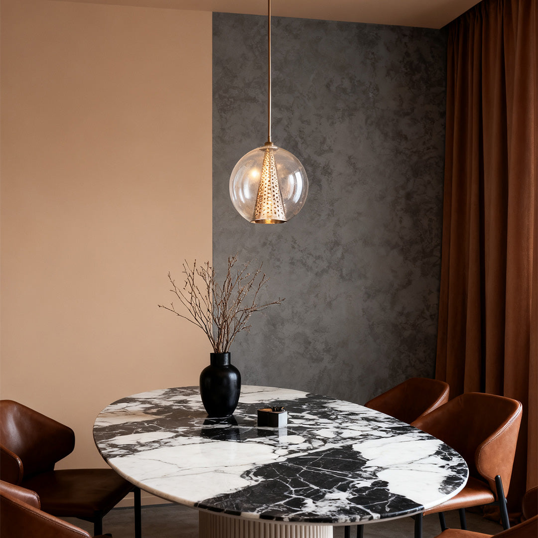 Single glass ball pendant lights with a clear shade and patterned brass interior, hanging over a black and white marble dining table.