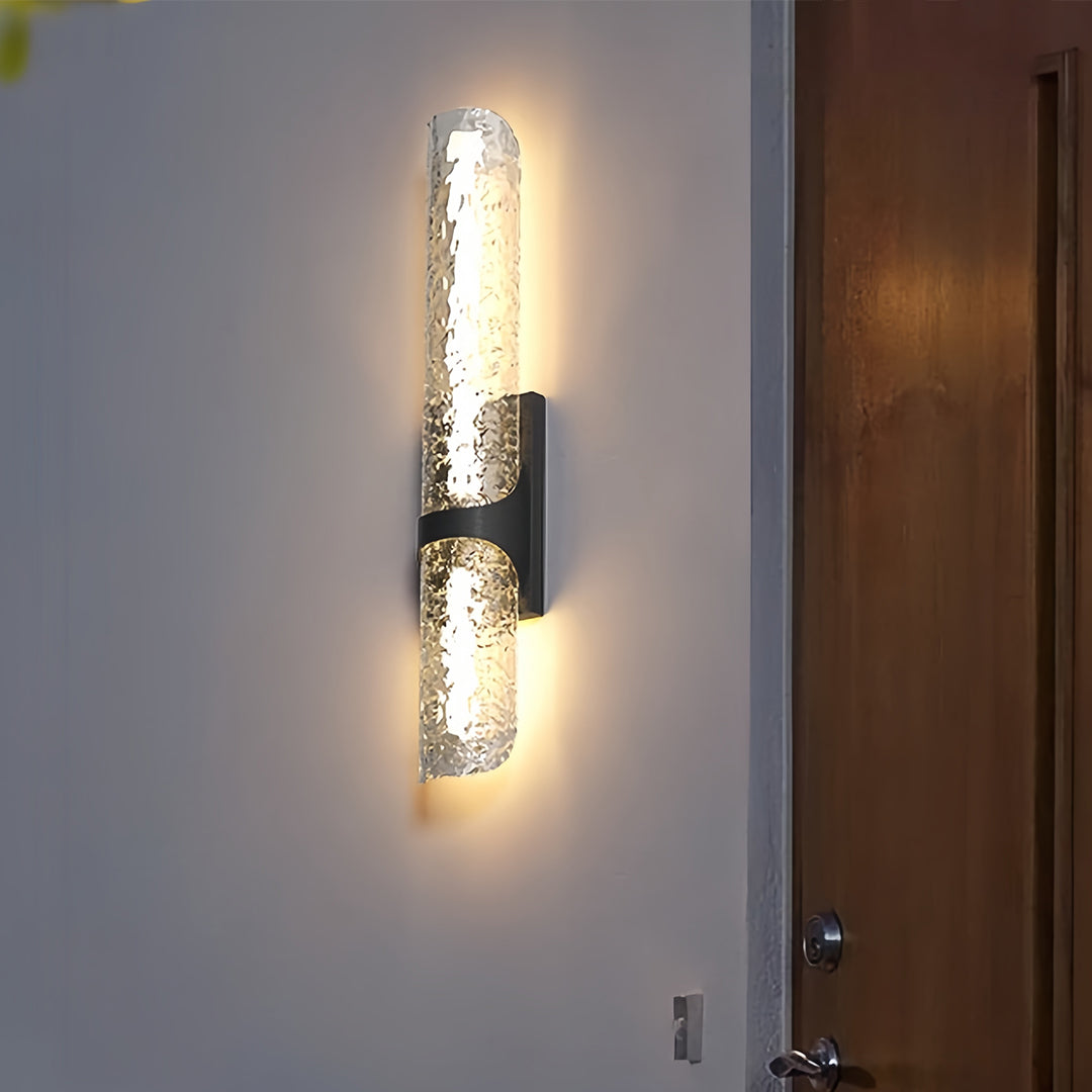 Single contemporary black outdoor wall light with textured ice glass installed on a plain wall next to a wooden door.