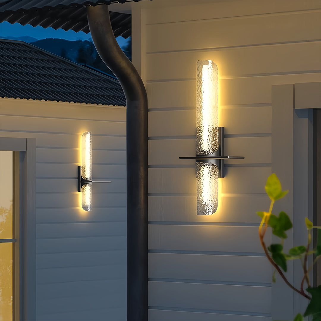 Single contemporary black outdoor wall light with a textured glass shade mounted on a home's siding.