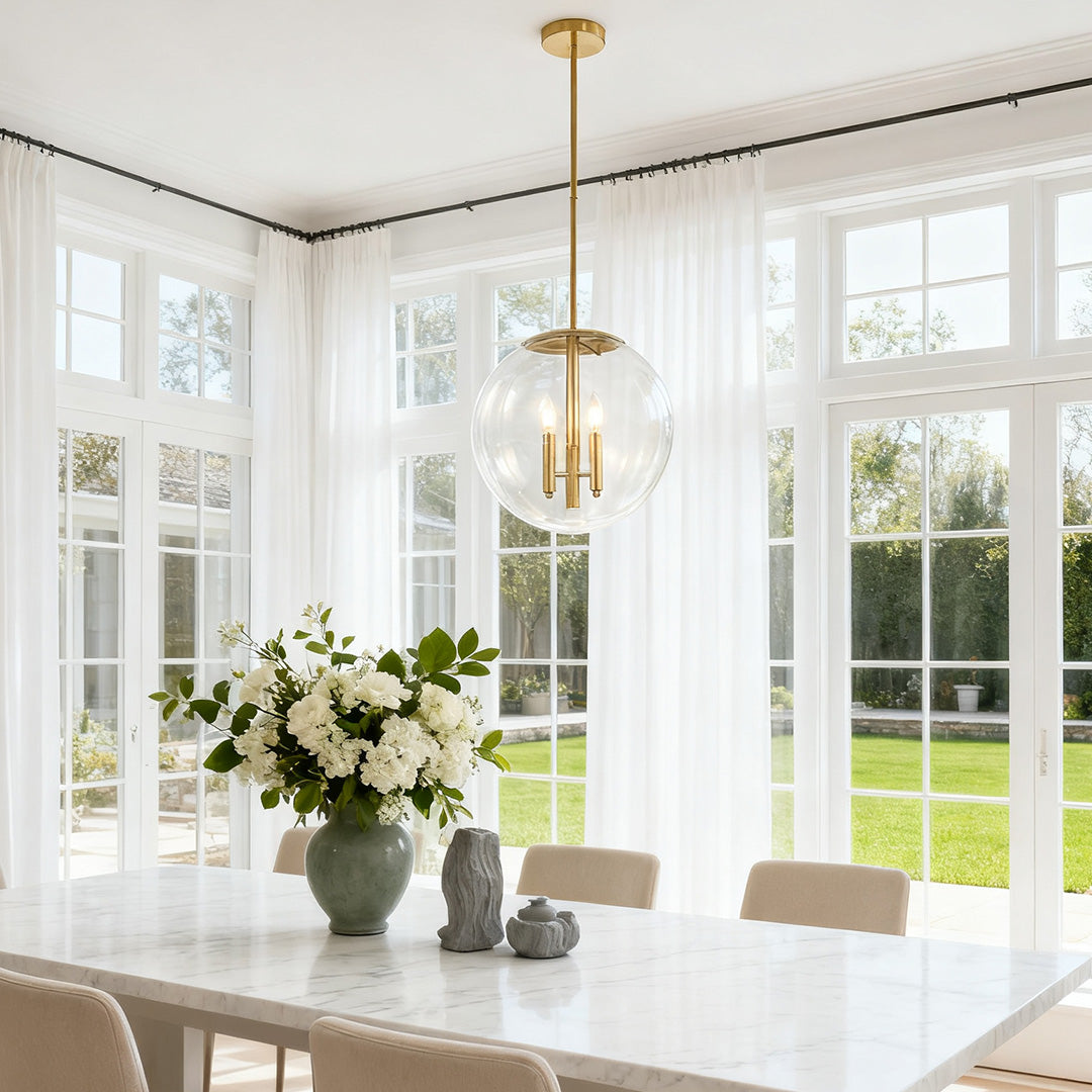 Single elegant clear globe pendant light providing bright illumination above a large white dining table near expansive windows.