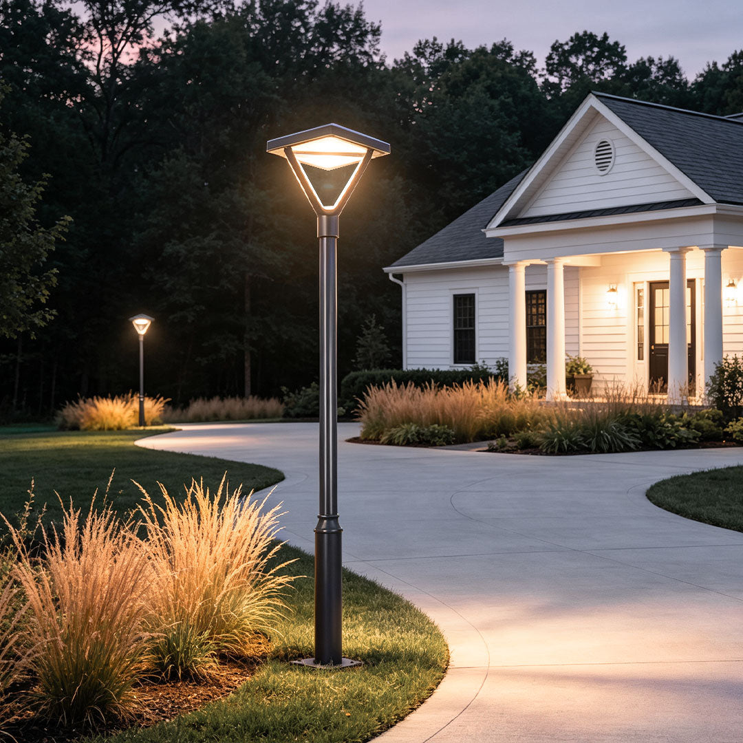 Single garden street light brightening a winding pathway near a white house and ornamental grass.