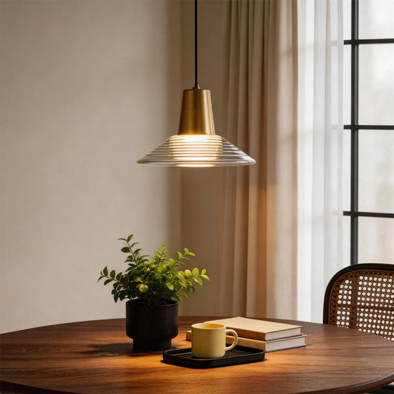 A single glass cone pendant light glowing warmly over a round wooden table by a bright window.