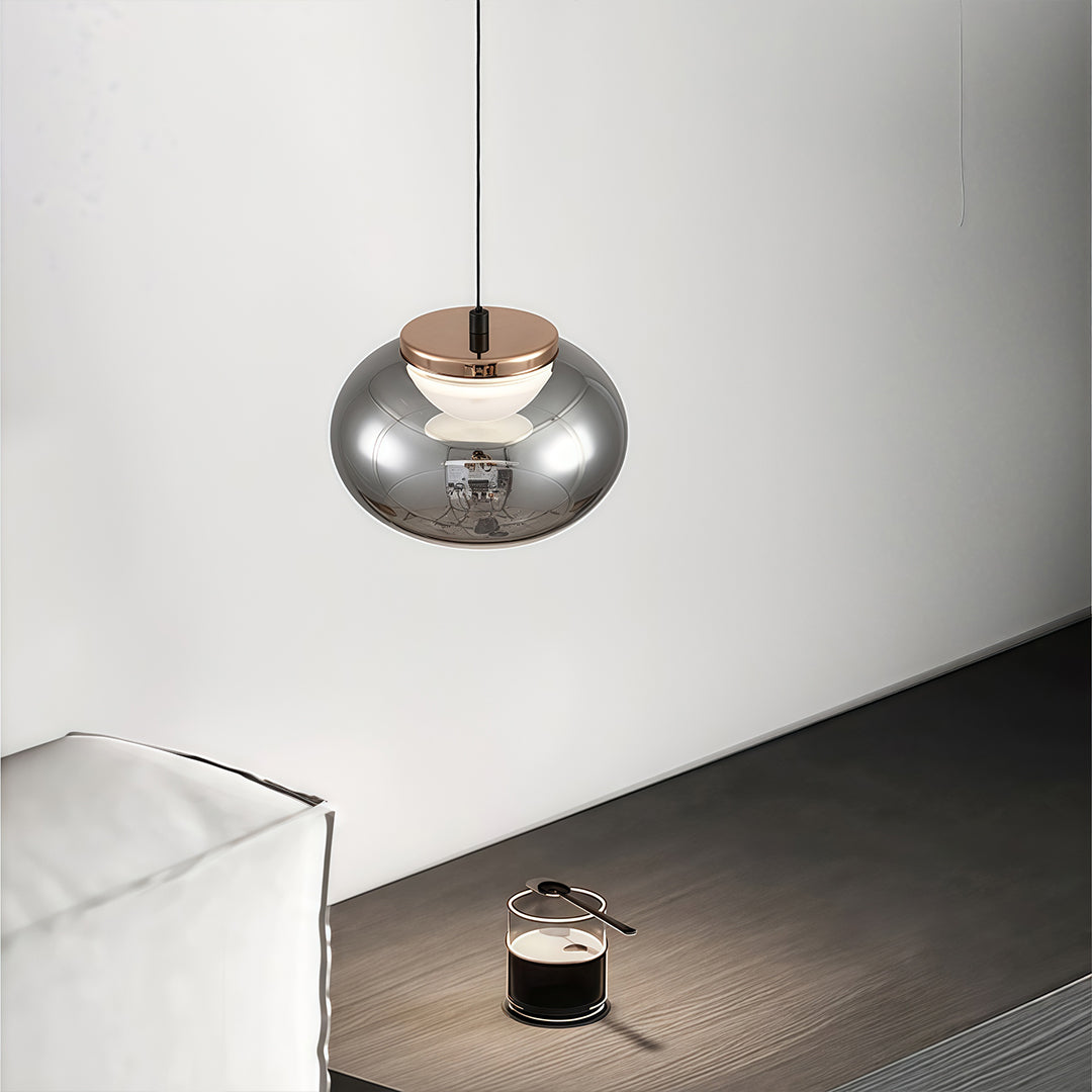 Single gray glass pendant light with chrome finish illuminating minimalist white wall and surface.
