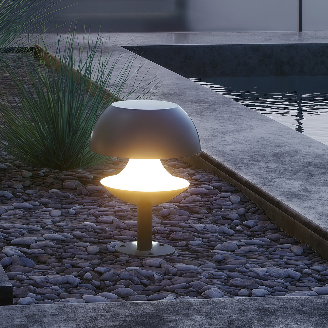 Single mushroom path light casting warm glow on stone paver pathway near water feature.