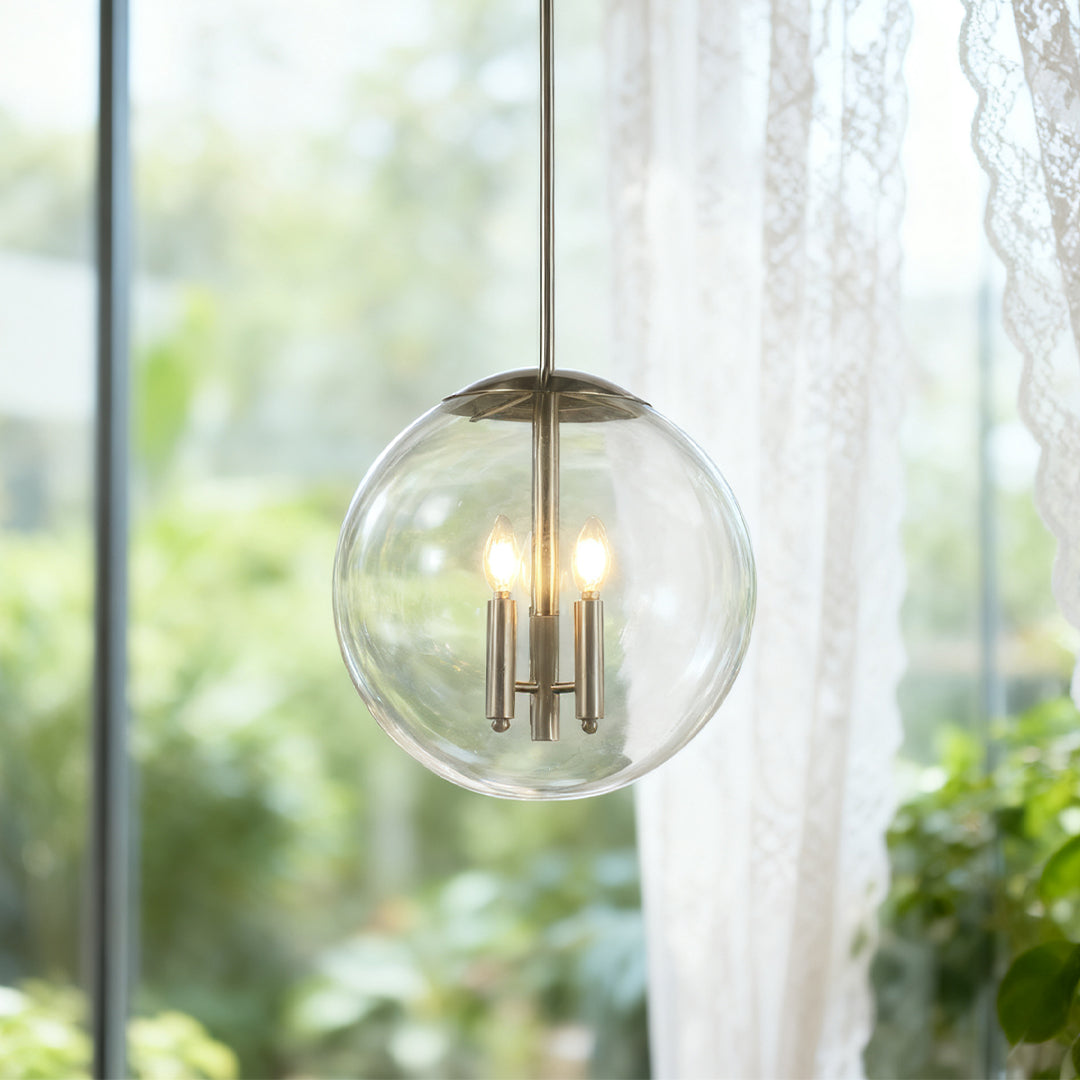 Modern single glass orb pendant light with nickel finish, featuring a three-light cluster inside, hanging by a bright lace-curtained window.