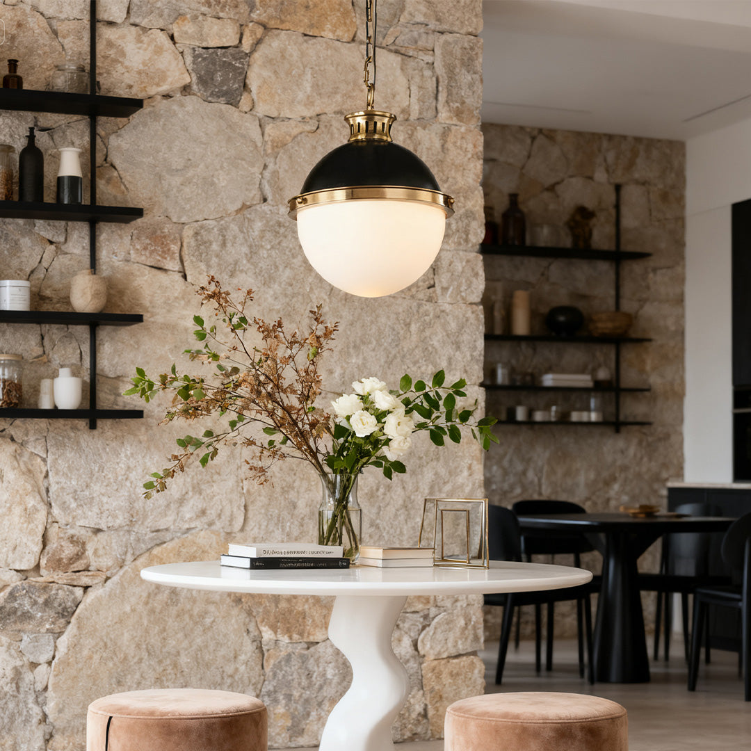 Single opal glass ball pendant light with black cap and brass chain, illuminating a round table against a rustic stone wall.