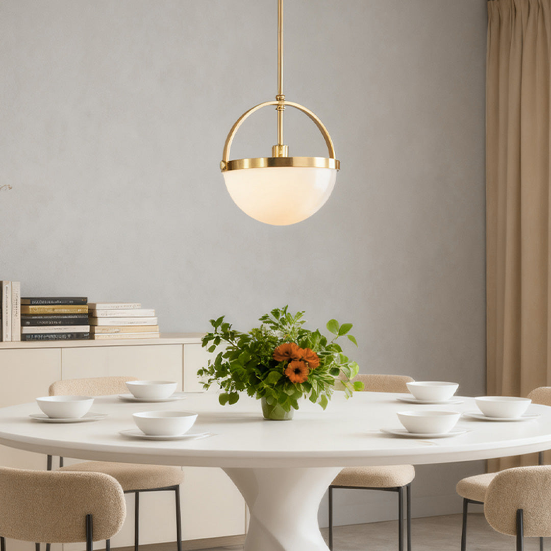 Single gold and white pendant light with an opal glass sphere, casting soft light over a minimalist white table in a bright, airy space.