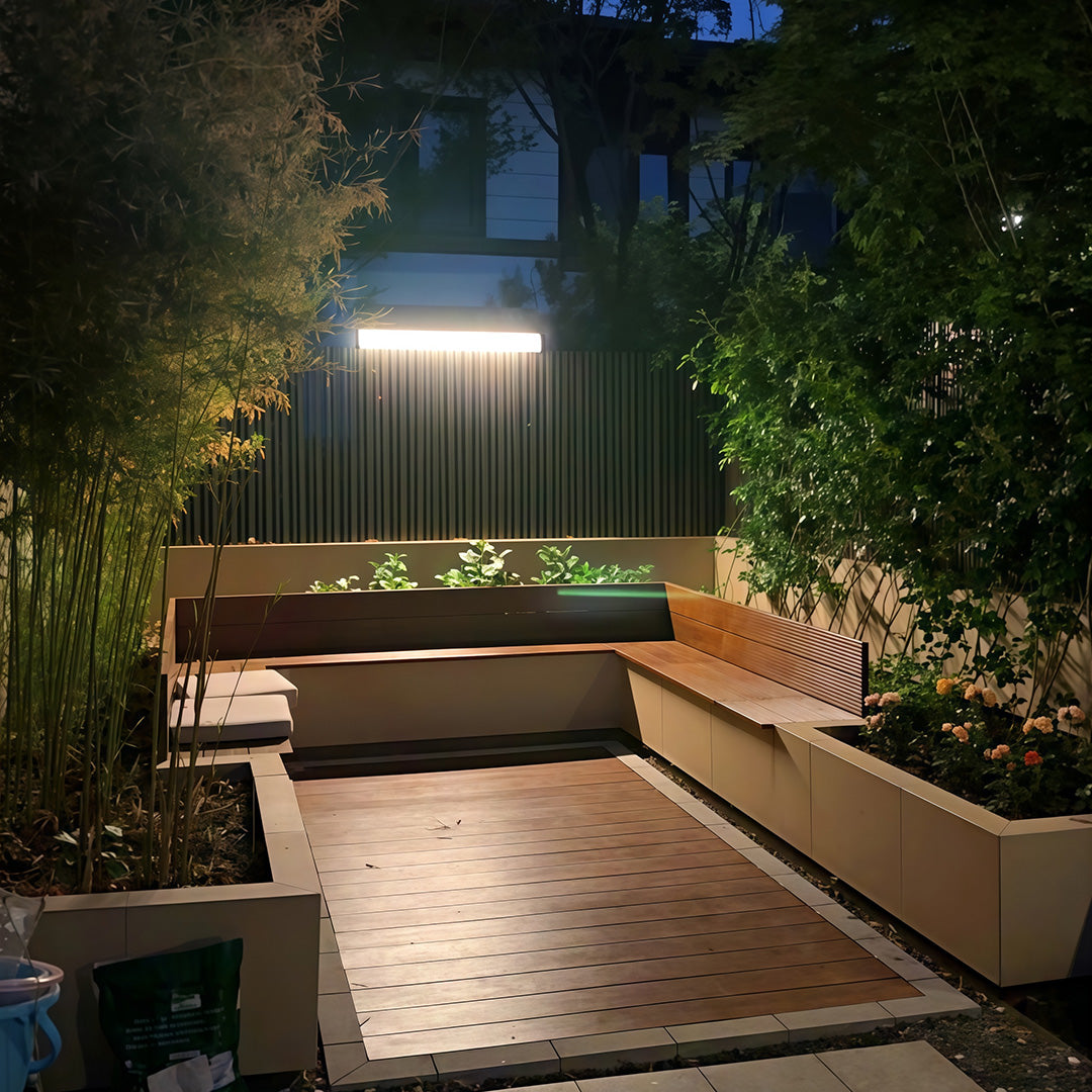 Single outdoor wall lighting modern bar mounted on a dark slatted fence in a garden.