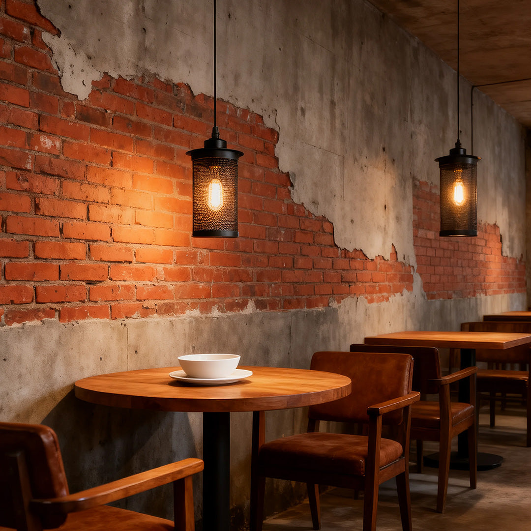 Single retro industrial pendant lights with a black wire cage casting warm light over a wooden cafe table and distressed brick wall.